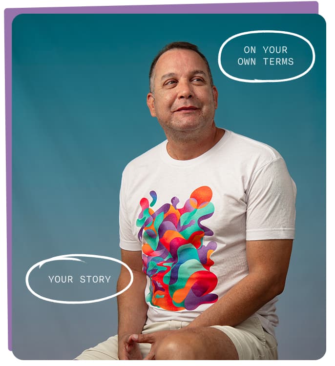 Man looking to the right and wearing a white t-shirt printed with colorful abstract artwork of figures and flowing shapes against a teal background